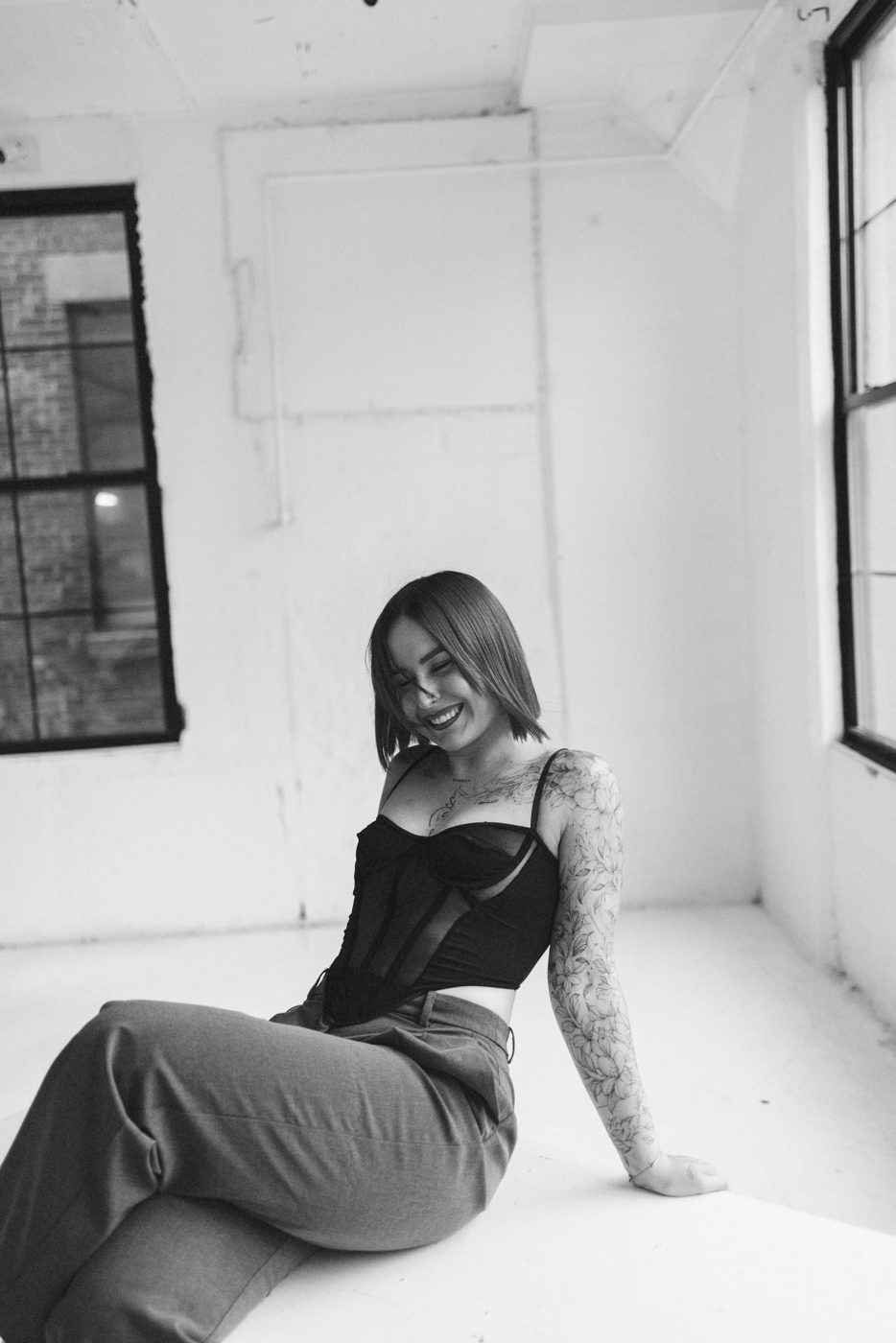 Laughing woman with a tattooed arm sitting on the floor of a white studio